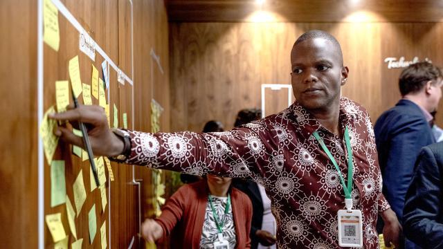 Jeune homme africain plaçant son idée écrite sur un post-it sur le tableau au mur