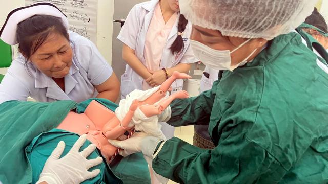Practical training for midwives. A student practises breech birth with a doll under the supervision of a midwife.