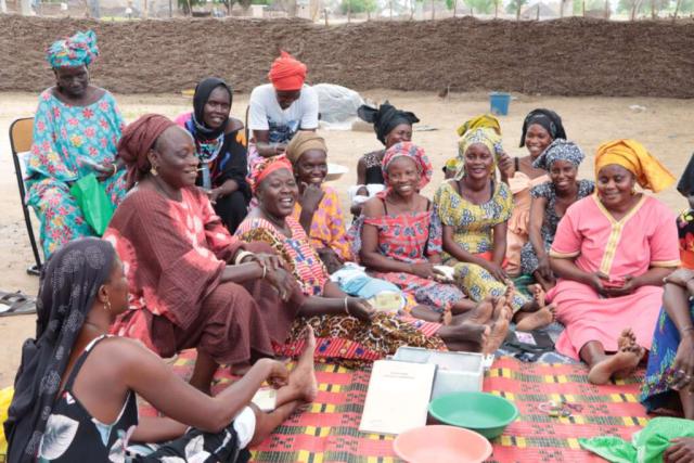 Groupe de femmes souriantes, membres de l'AVECi de Barkaël, assises en cercle sur le sol