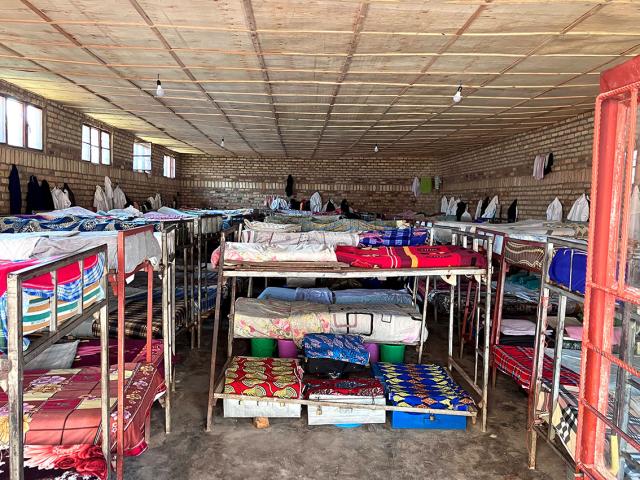 A dormitory in Rwanda which has rows of bunk beds with colorful blankets inside a brick building.