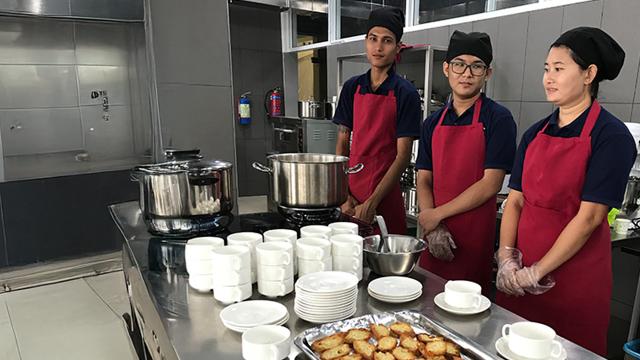 Trois apprentis cuisinier se tiennent derrière un plan de travail où se trouvent des tasses et des toasts