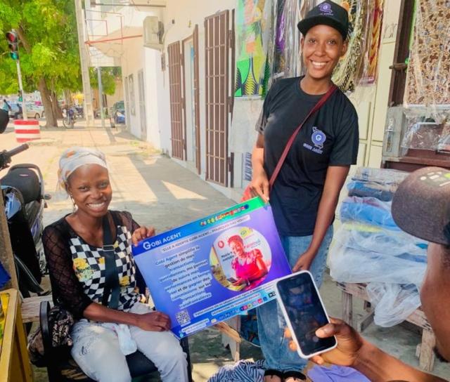 deux femmes souriantes et un homme devant elles utilisant son téléphone portable